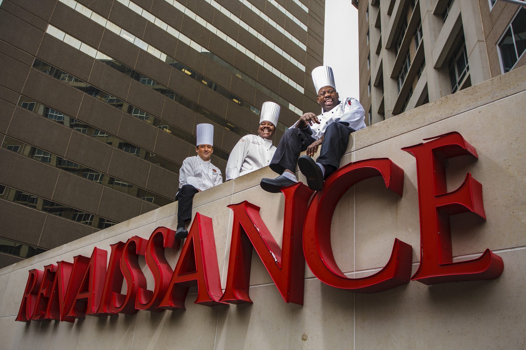 Three chefs seated on a hotel sign above the street