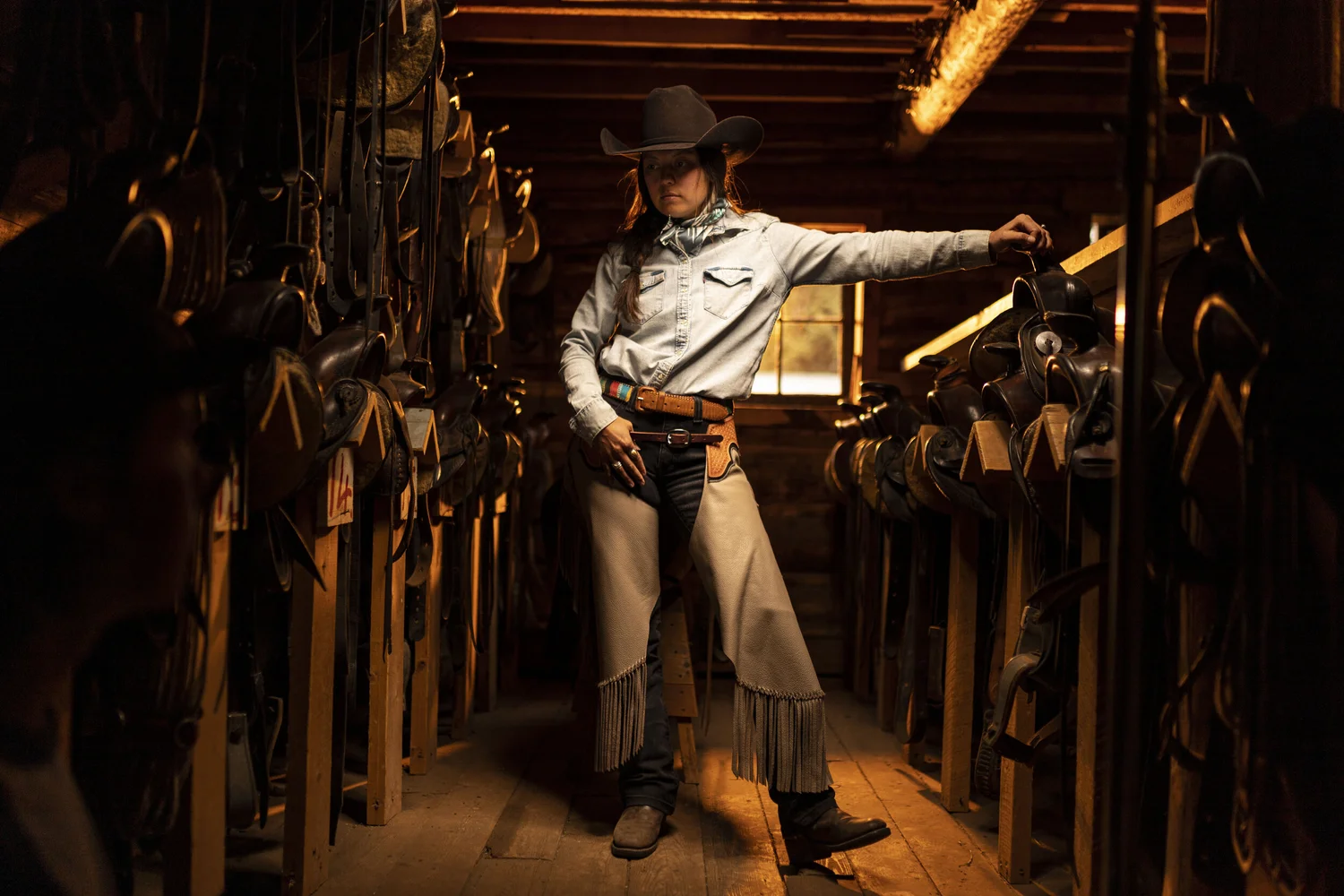 Horsewoman standing in a tack room at the edge of window light