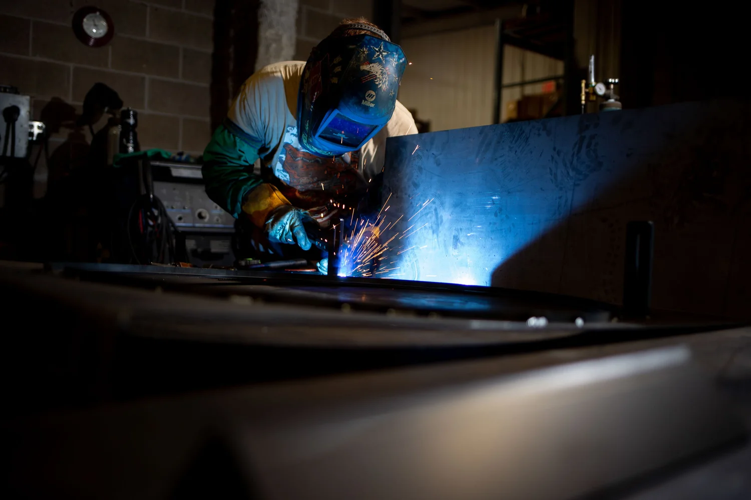 Welder working in a dark shop with blue light and flying sparks